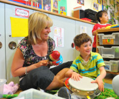 Teacher and student playing instruments on floor in classroom.