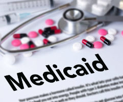 Document with medicaid as heading, stethoscope layin on top with pills spilled on top.