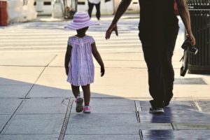 Small girl with matching hat walking with parent on city street.