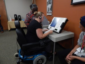 Voter in wheelchair uses accessible voting machine with others looking on