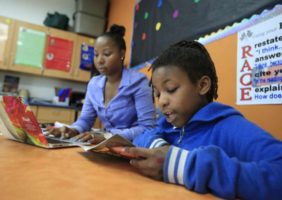 Student at Racine school reading with teacher in background